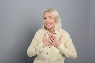 Photo of Happy woman holding hands near heart on grey background