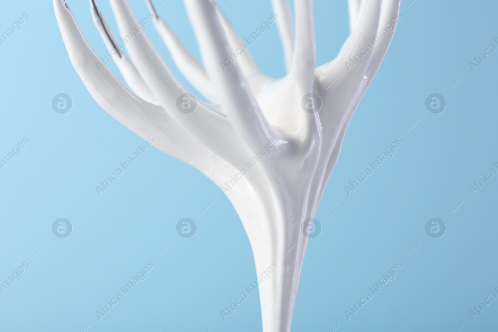 Photo of Whisk with whipped cream on light blue background, closeup