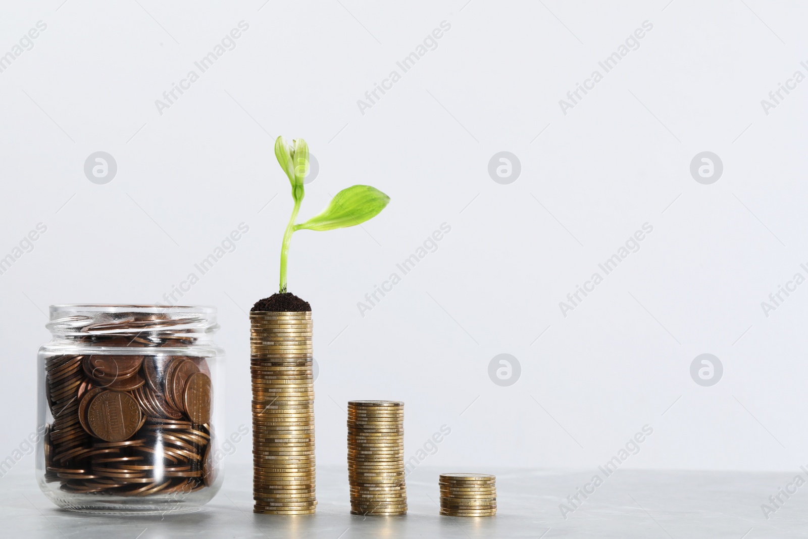 Photo of Glass jar with coins and flower on grey table, space for text. Investment concept