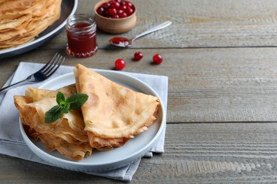 Photo of Delicious crepes served with mint on grey wooden table. Space for text