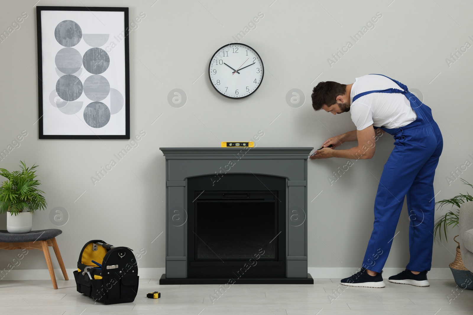 Photo of Professional technician with screwdriver installing electric fireplace in room