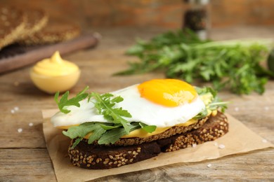 Photo of Delicious sandwich with arugula and fried egg on wooden table