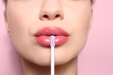 Photo of Beautiful young woman applying gloss on her perfect lips, closeup
