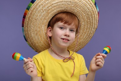 Photo of Cute boy in Mexican sombrero hat with maracas on violet background