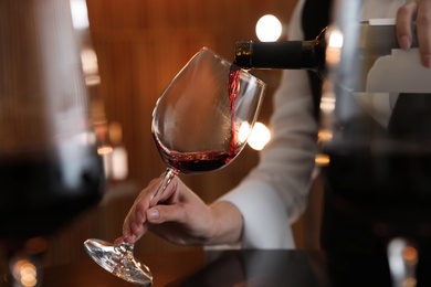 Waitress pouring wine into glass in restaurant, closeup