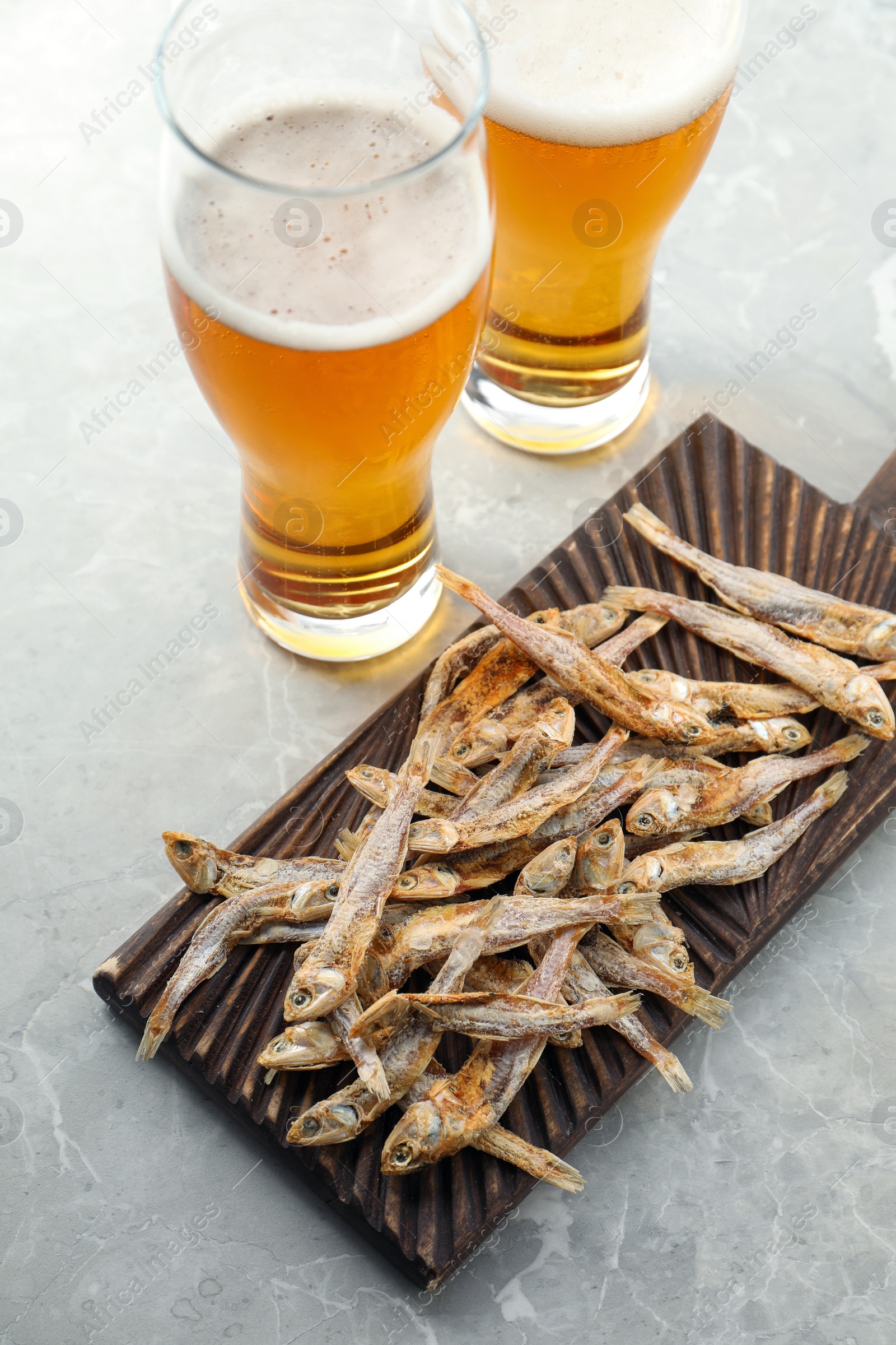 Photo of Delicious dried anchovies near glasses of beer on light marble table