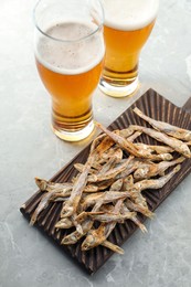 Delicious dried anchovies near glasses of beer on light marble table