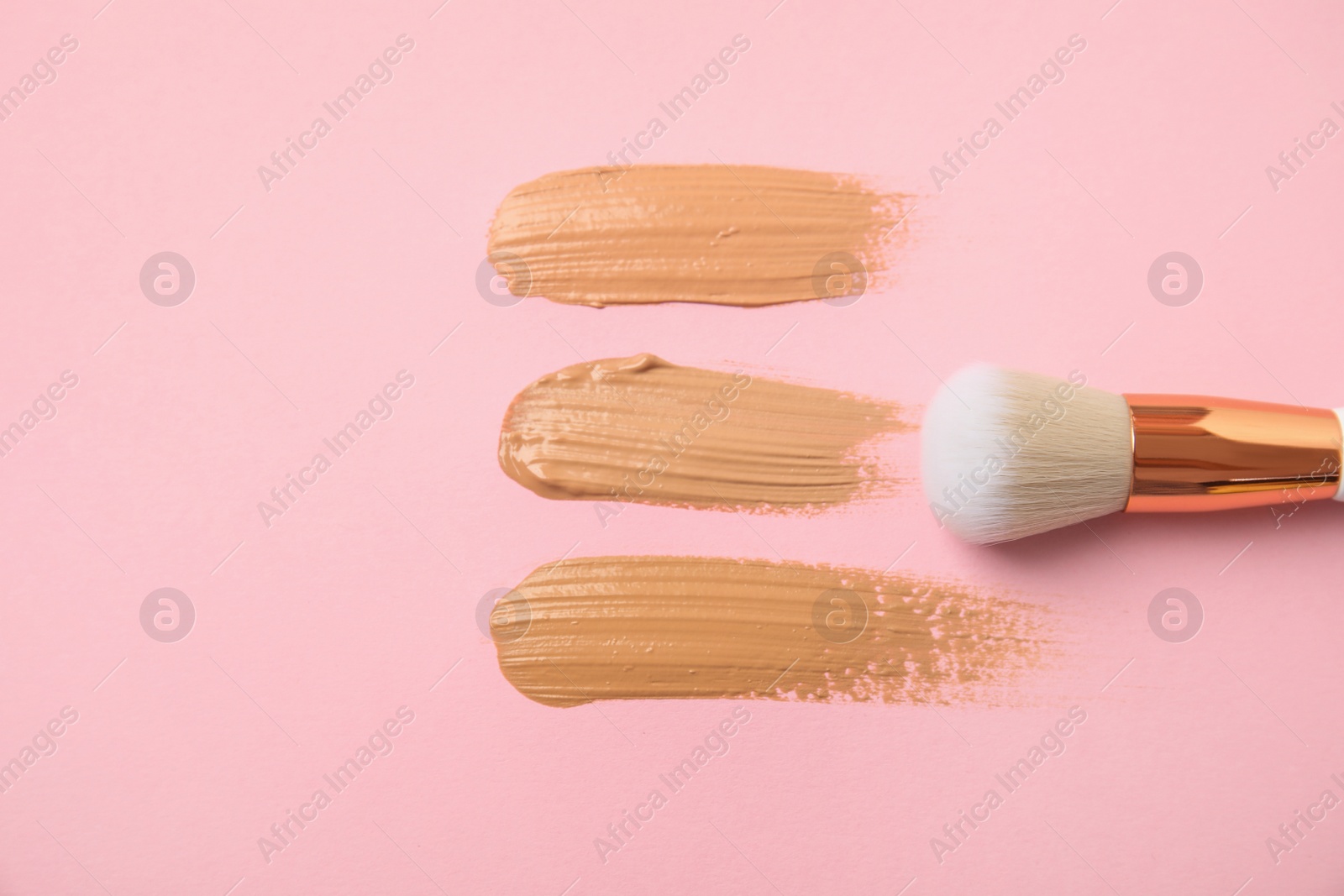 Photo of Samples of different foundation shades and makeup brush on pink background, above view