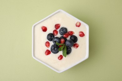 Photo of Bowl of delicious semolina pudding with blueberries, pomegranate and mint on light green background, top view