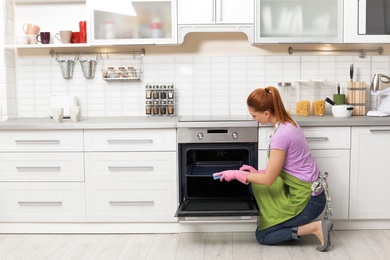 Photo of Woman cleaning oven tray with rag in kitchen