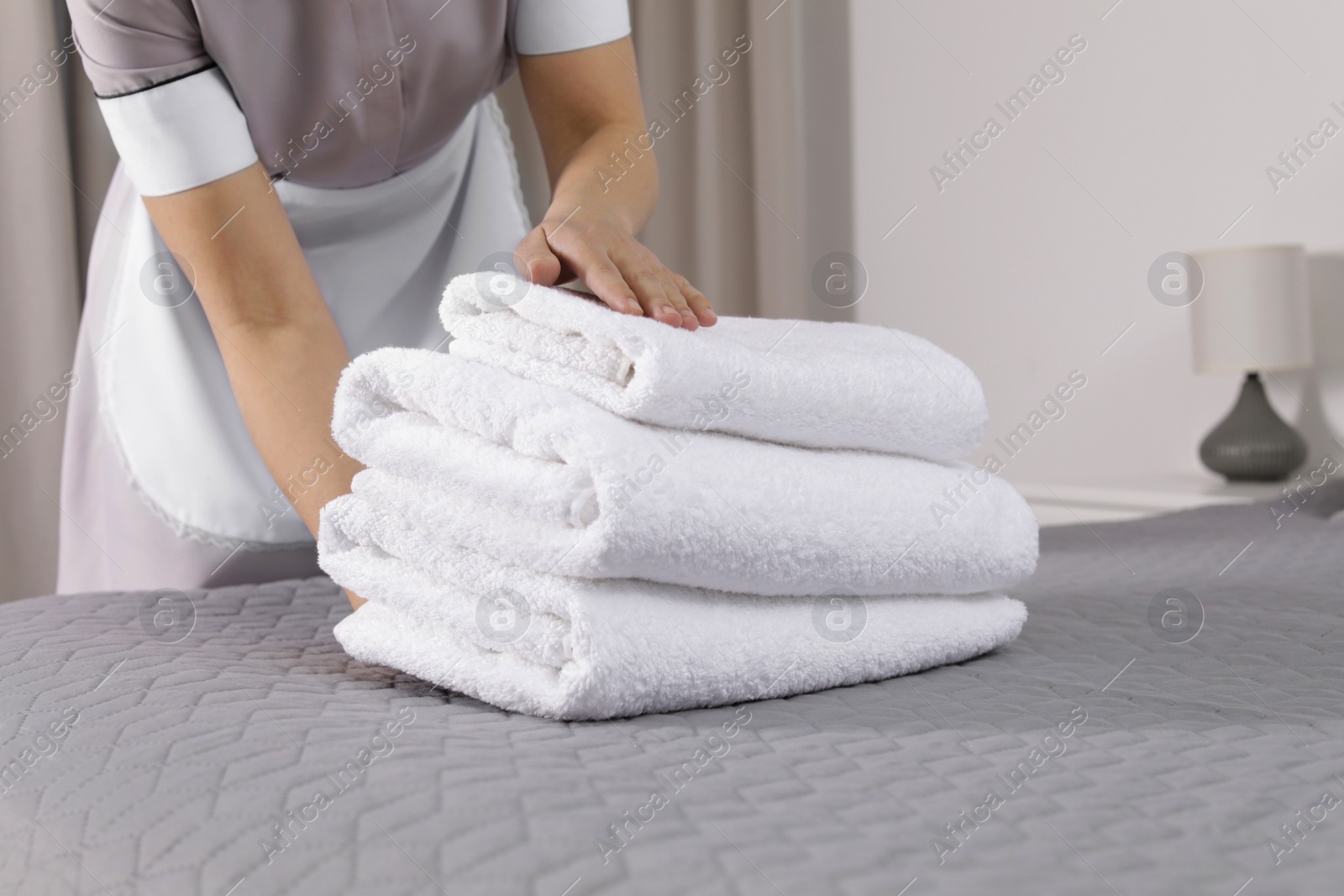 Photo of Maid putting fresh towels on bed in hotel room, closeup