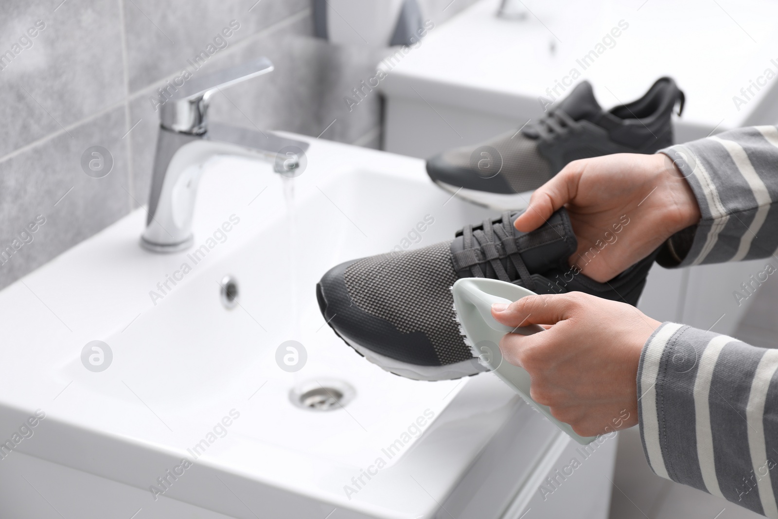 Photo of Woman washing stylish sneakers with brush in sink, closeup