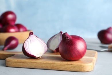 Photo of Wooden cutting board with red onions on grey table