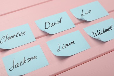 Photo of Paper stickers with different names on pink wooden table, closeup. Choosing baby's name