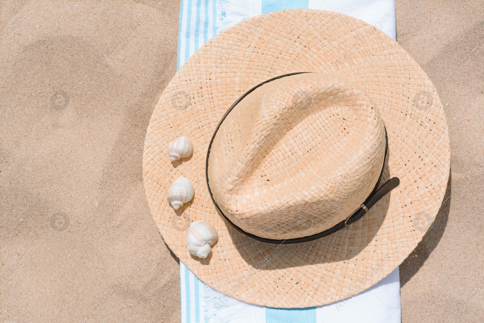 Photo of Straw hat with seashells and beach towel on sand, top view. Space for text