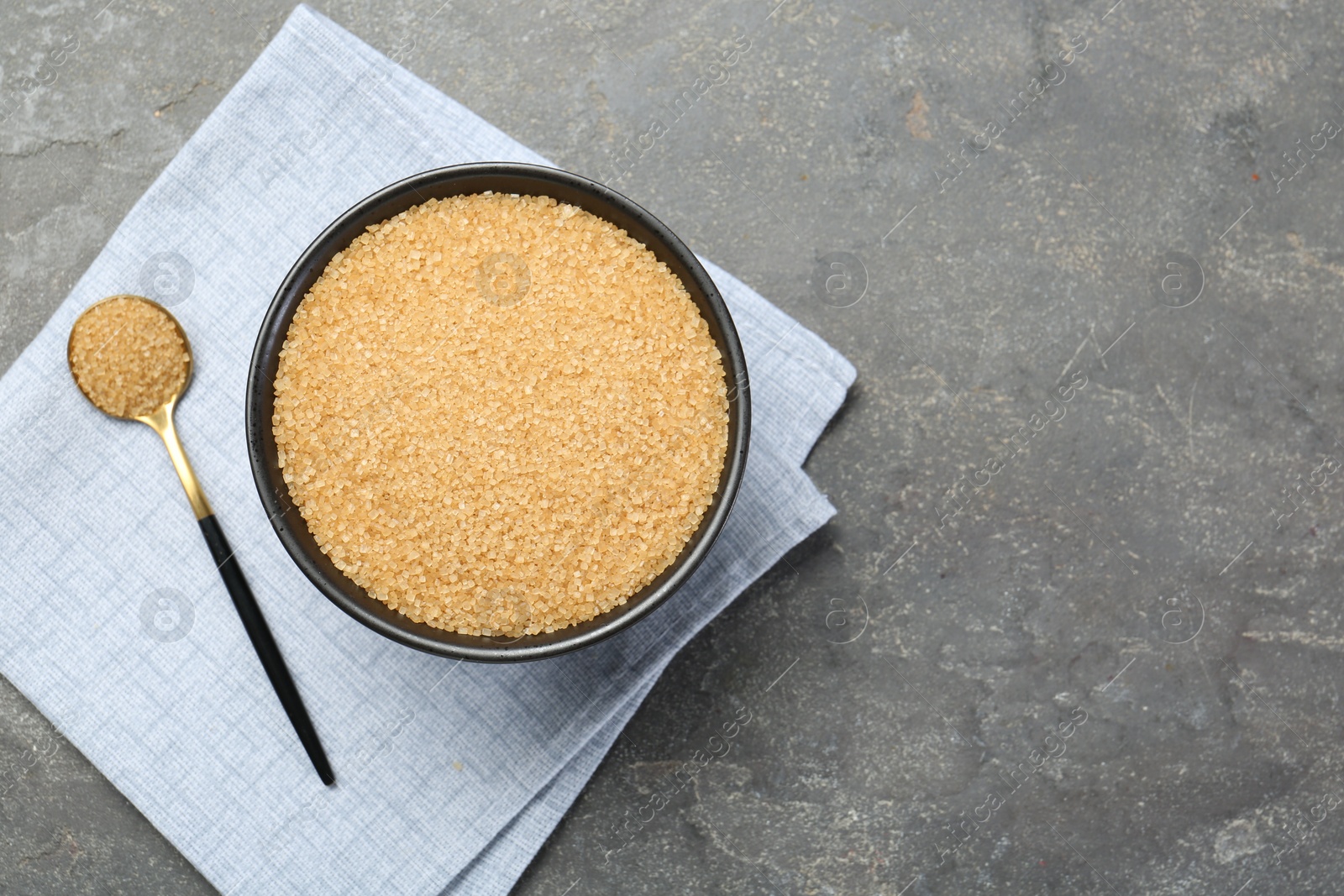 Photo of Brown sugar in bowl and spoon on grey textured table, top view. Space for text