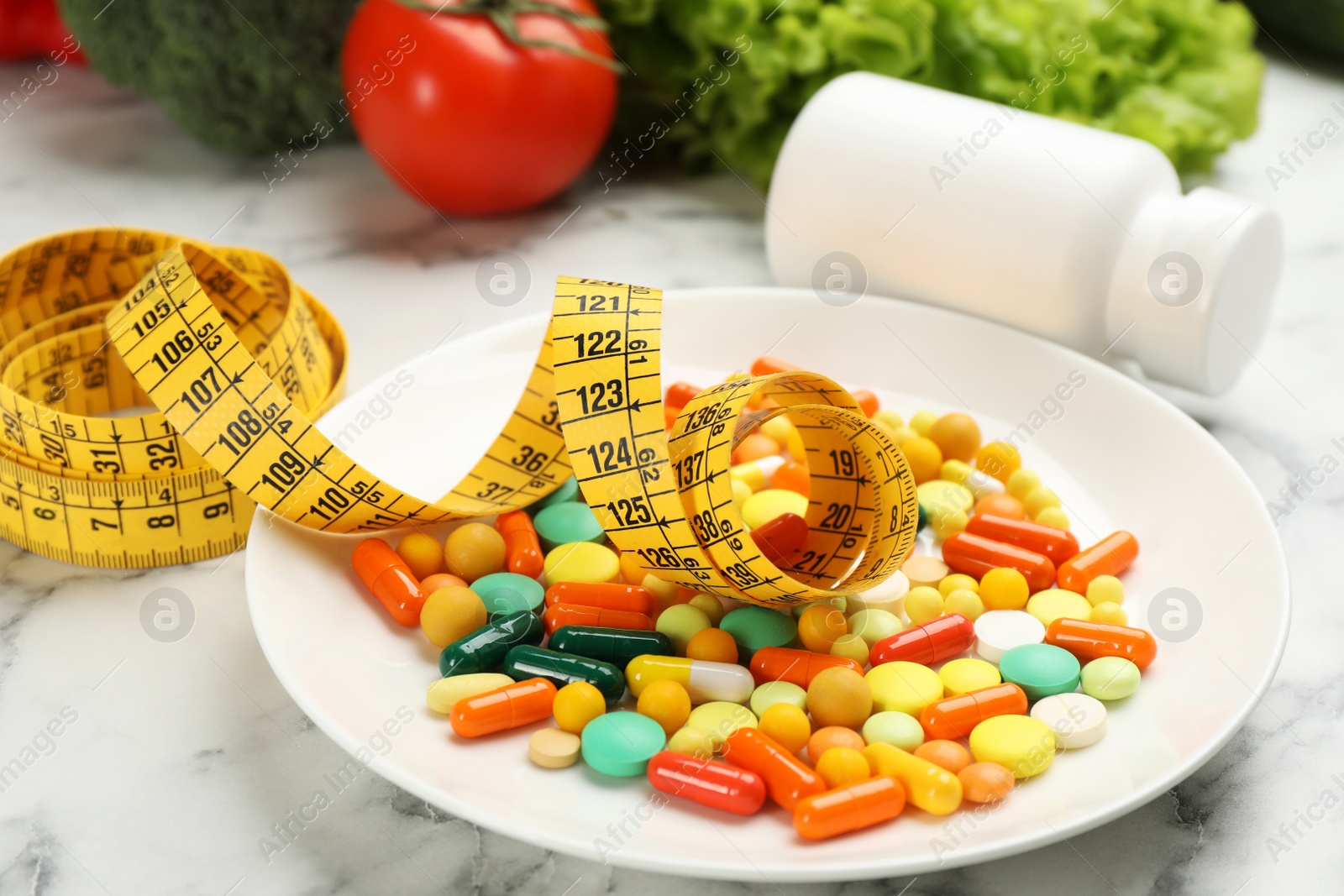 Photo of Plate with different weight loss pills and measuring tape on white marble table