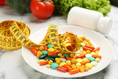 Photo of Plate with different weight loss pills and measuring tape on white marble table