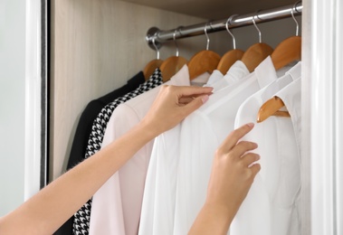 Photo of Woman taking shirt from wardrobe with stylish clothes, closeup view
