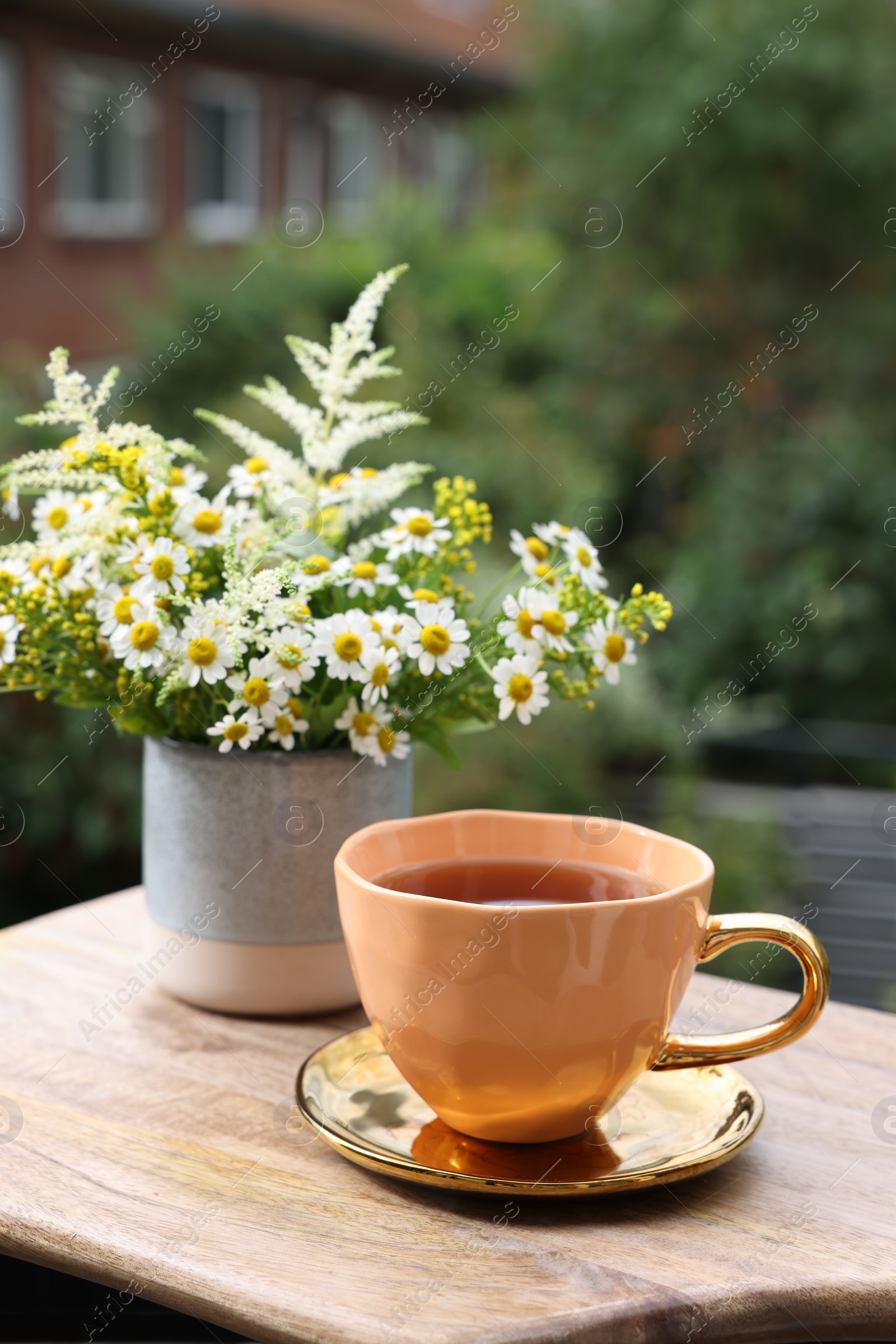 Photo of Cup of delicious chamomile tea and fresh flowers outdoors