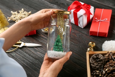 Photo of Woman making snow globe at black wooden table, closeup