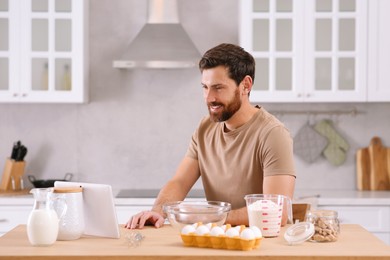 Man making dough while watching online cooking course via tablet in kitchen