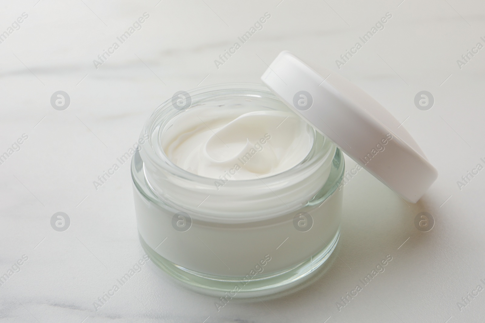 Photo of Glass jar of face cream on white marble table