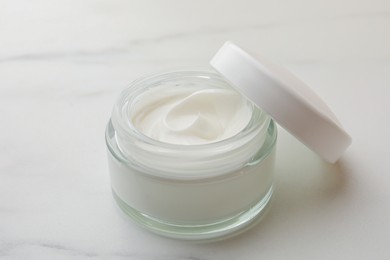 Glass jar of face cream on white marble table