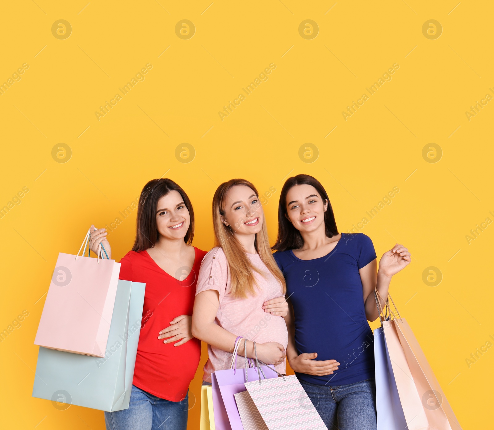 Photo of Happy pregnant women with shopping bags on orange background