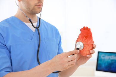 Photo of Male doctor with heart model and stethoscope in clinic. Cardiology center