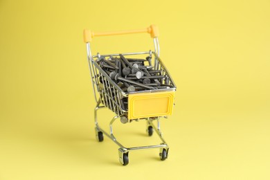 Metal nails in shopping cart on yellow background