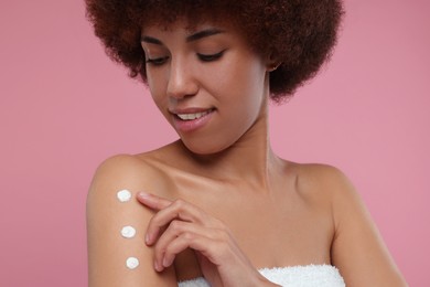 Photo of Beautiful young woman applying body cream onto arm on pink background