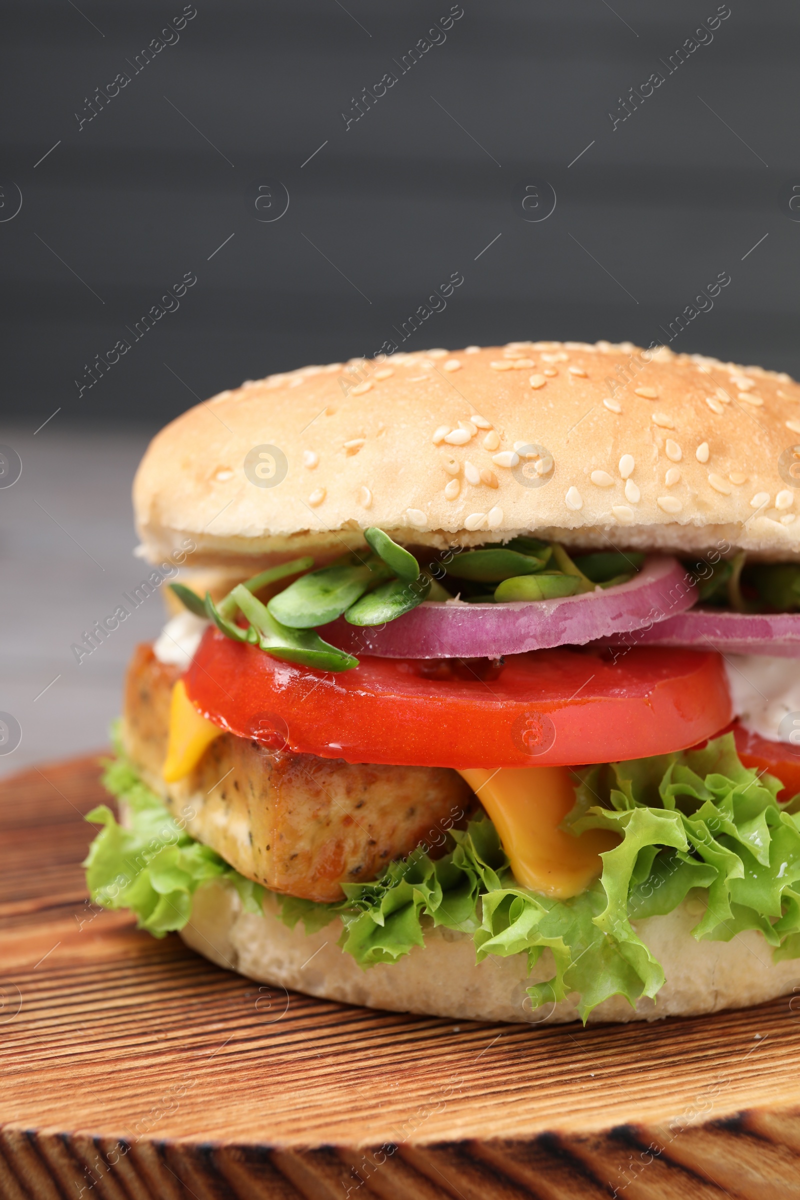 Photo of Delicious burger with tofu and fresh vegetables on wooden board, closeup