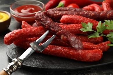 Photo of Thin dry smoked sausages and fork on dark table, closeup