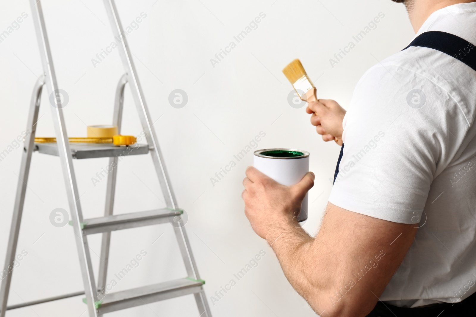 Photo of Male decorator with brush and paint can indoors, closeup. Space for text