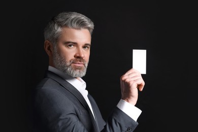 Photo of Handsome businessman holding blank business card on black background