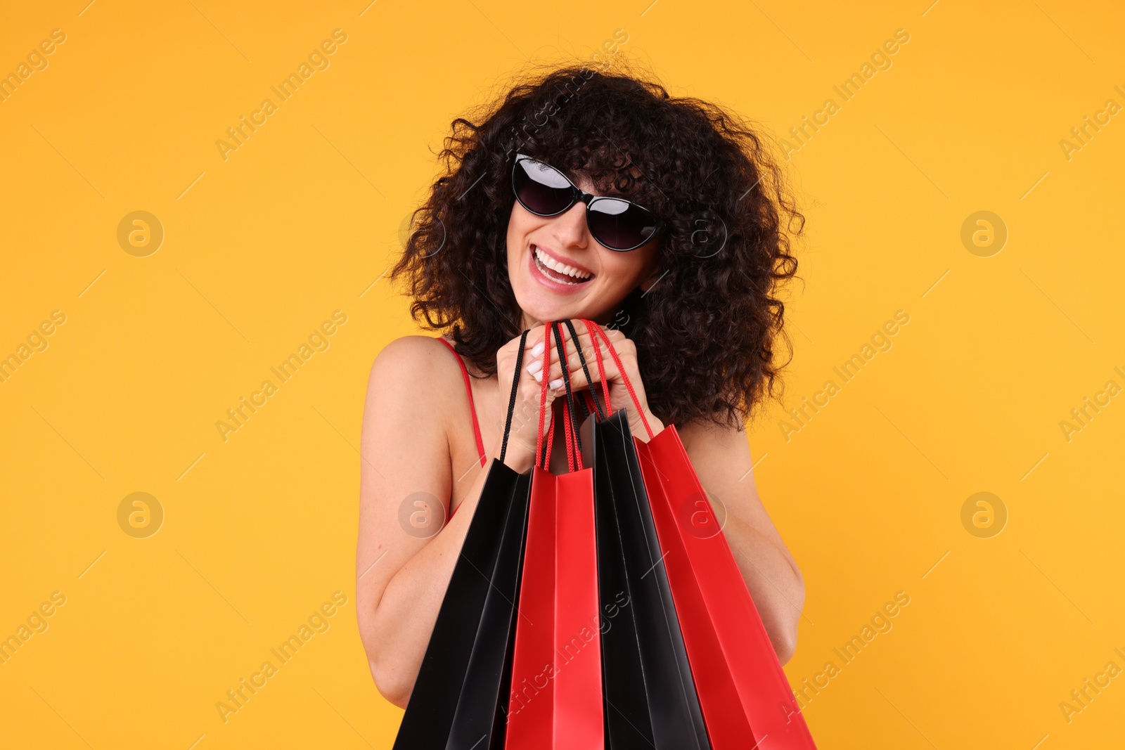 Photo of Happy young woman with shopping bags and stylish sunglasses on yellow background