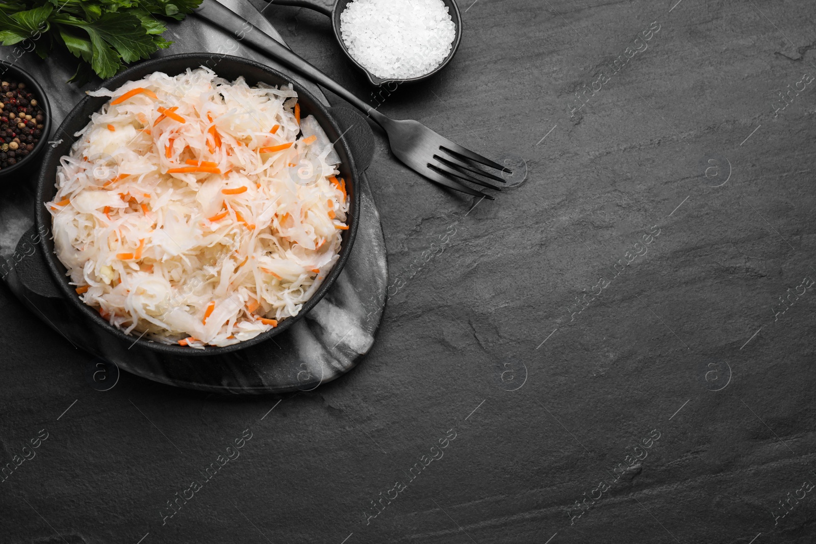 Photo of Bowl of tasty sauerkraut and ingredients on black table, flat lay. Space for text