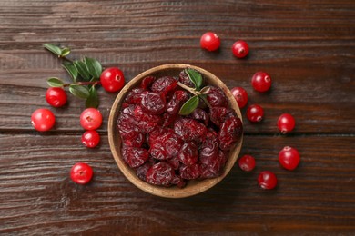 Tasty dried cranberries in bowl, fresh ones and leaves on wooden table, top view