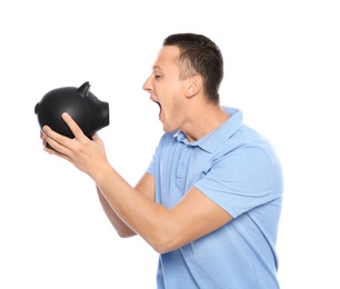 Emotional young man with piggy bank on white background