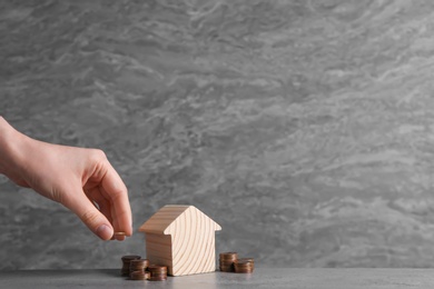 Photo of Woman putting coin near house model on table against grey background. Space for text