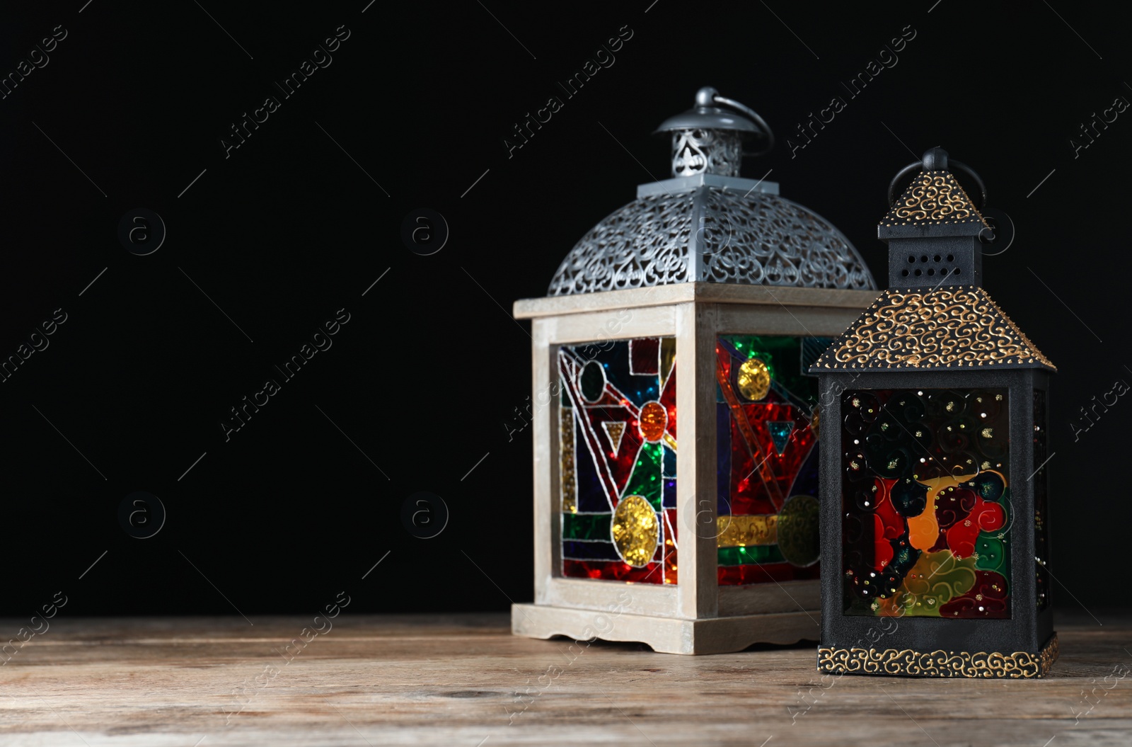 Photo of Decorative Arabic lanterns on wooden table against black background, space for text