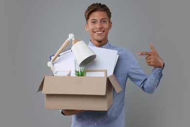Photo of Happy unemployed young man with box of personal office belongings on grey background
