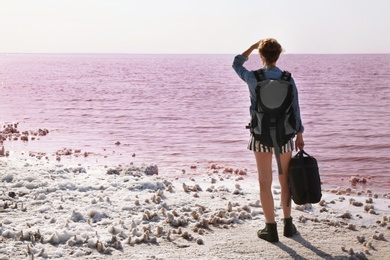 Photo of Woman with backpack and sleeping bag on coast of pink lake