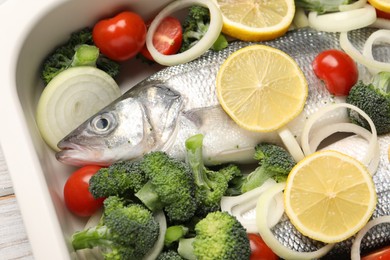 Photo of Raw fish with vegetables and lemon in baking dish on table