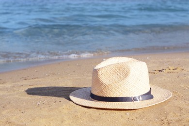 Stylish straw hat on sandy beach near sea