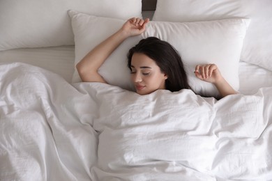 Photo of Young woman covered with warm white blanket sleeping in bed, top view