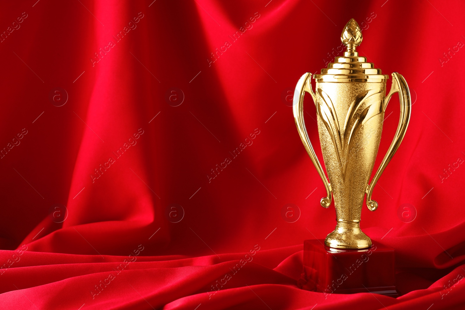 Photo of Golden trophy cup on red fabric. Space for text