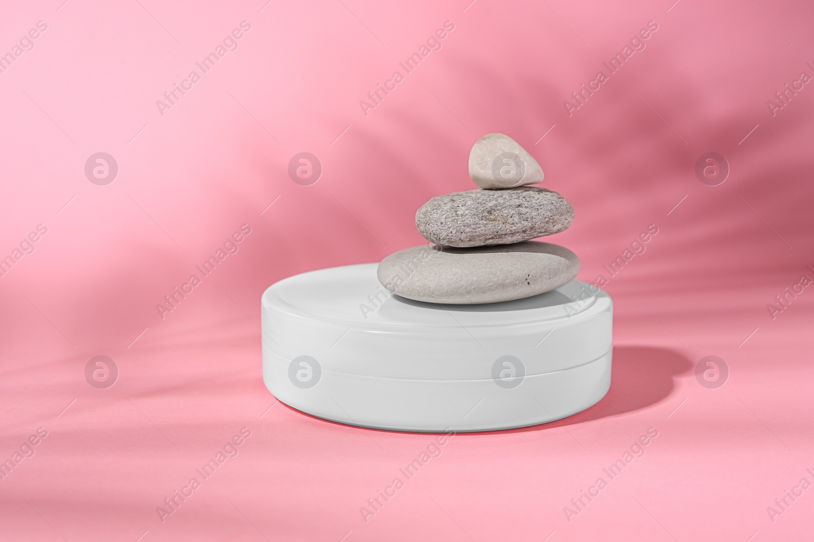 Photo of Cosmetic product, stacked stones and shadow of tropical leaf on pink background