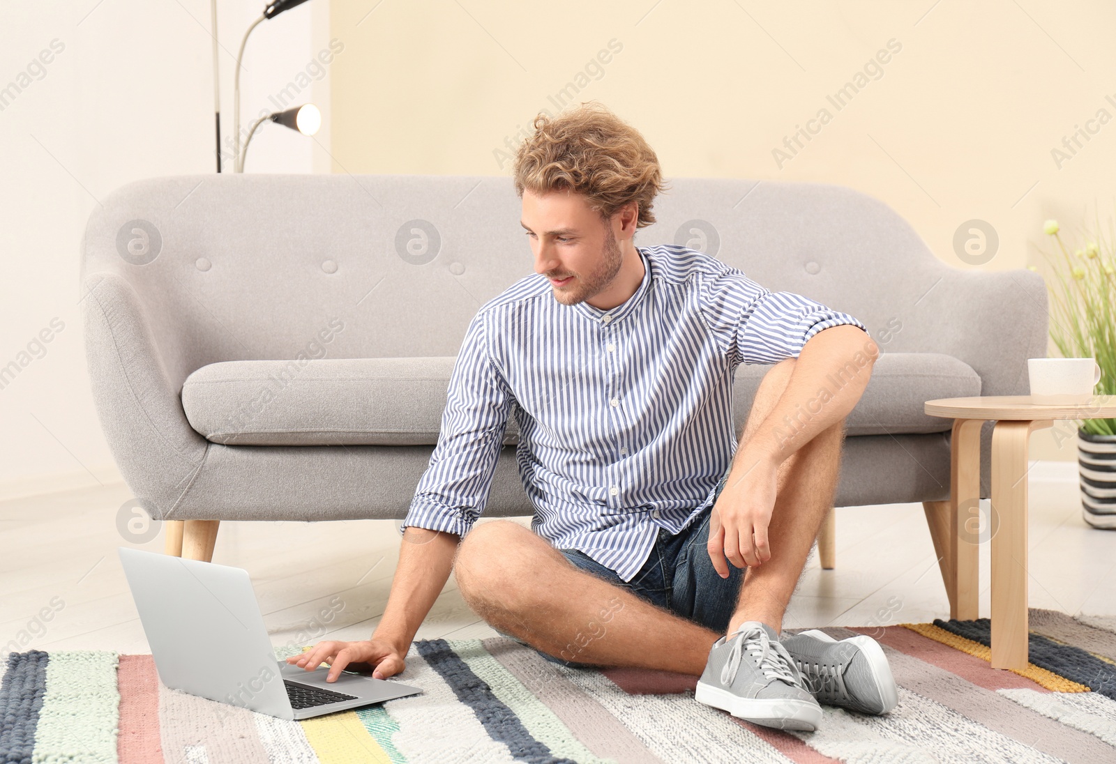 Photo of Young man with laptop sitting on floor at home